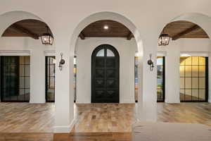 Entryway with a wood ceiling with exposed beams, arched walkways, a chandelier, and light wood-type flooring