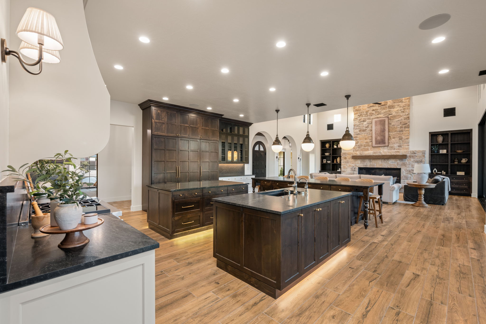 Kitchen with pendant lighting, dark wood finish cabinets, a stone fireplace, glass fronted cabinets, and open floor plan