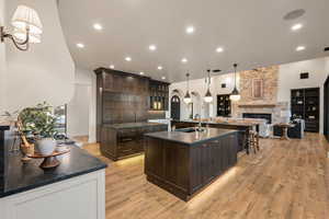 Kitchen with pendant lighting, dark wood finish cabinets, a stone fireplace, glass fronted cabinets, and open floor plan