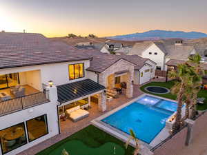 Rear view of house featuring a patio, an outdoor hangout area, an area to practice putting, stucco siding, and a pool with connected hot tub