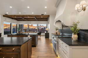 Kitchen featuring high end stainless steel range oven, beam ceiling, light wood finished floors, decorative backsplash, and dark stone countertops