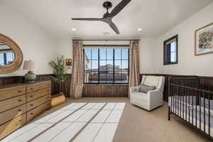 Bedroom with a nursery area, a wainscoted wall, wooden walls, light carpet, and ceiling fan