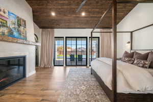 Bedroom with a vaulted wood ceiling, wood finished floors, a glass covered fireplace, access to outside, and recessed lighting