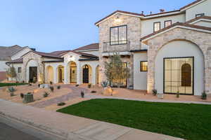 Mediterranean / spanish-style home featuring stucco siding, stone siding, a balcony, and a front lawn