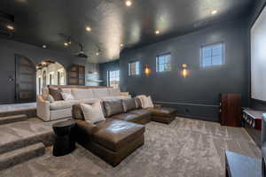 Home theater featuring arched walkways, carpet floors, a textured ceiling, and track lighting