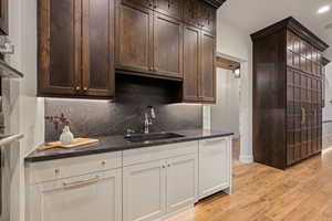 Kitchen featuring light wood-style flooring, dark wood finish cabinetry, dark stone counters, decorative backsplash, and recessed lighting