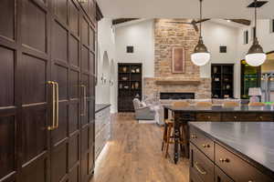 Kitchen featuring dark wood finish cabinetry, light wood finished floors, a stone fireplace, open floor plan, and pendant lighting