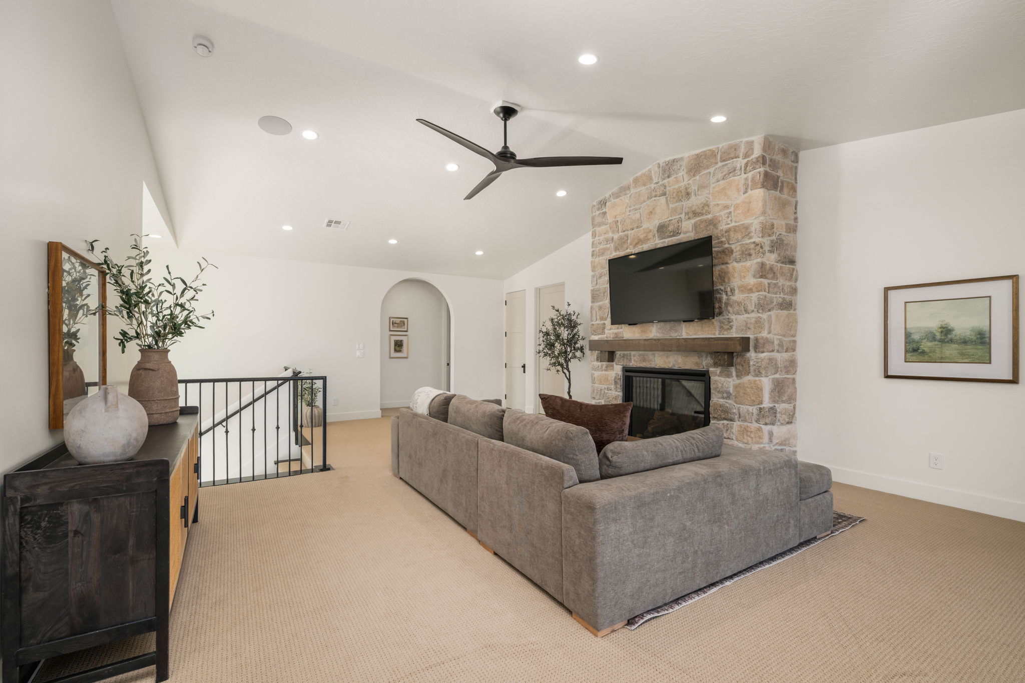Living area featuring ceiling fan, a stone fireplace, arched walkways, light colored carpet, and lofted ceiling