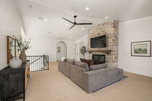 Living area featuring ceiling fan, a stone fireplace, arched walkways, light colored carpet, and lofted ceiling
