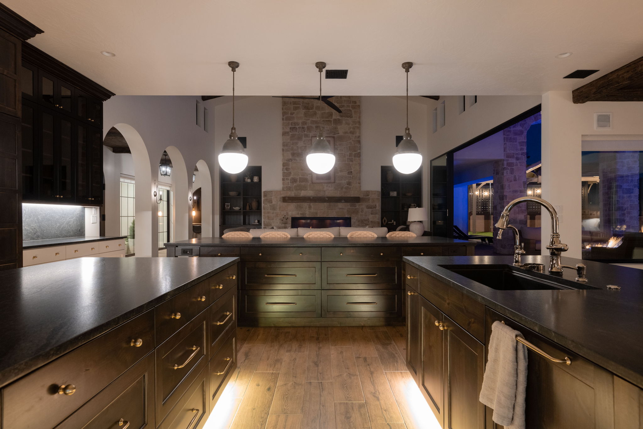 Kitchen with open floor plan, arched walkways, hanging light fixtures, light wood finished floors, and dark stone counters