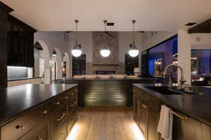 Kitchen with open floor plan, arched walkways, hanging light fixtures, light wood finished floors, and dark stone counters