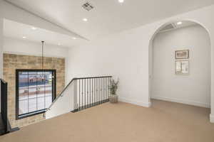 Empty room with light colored carpet, vaulted ceiling, arched walkways, and recessed lighting