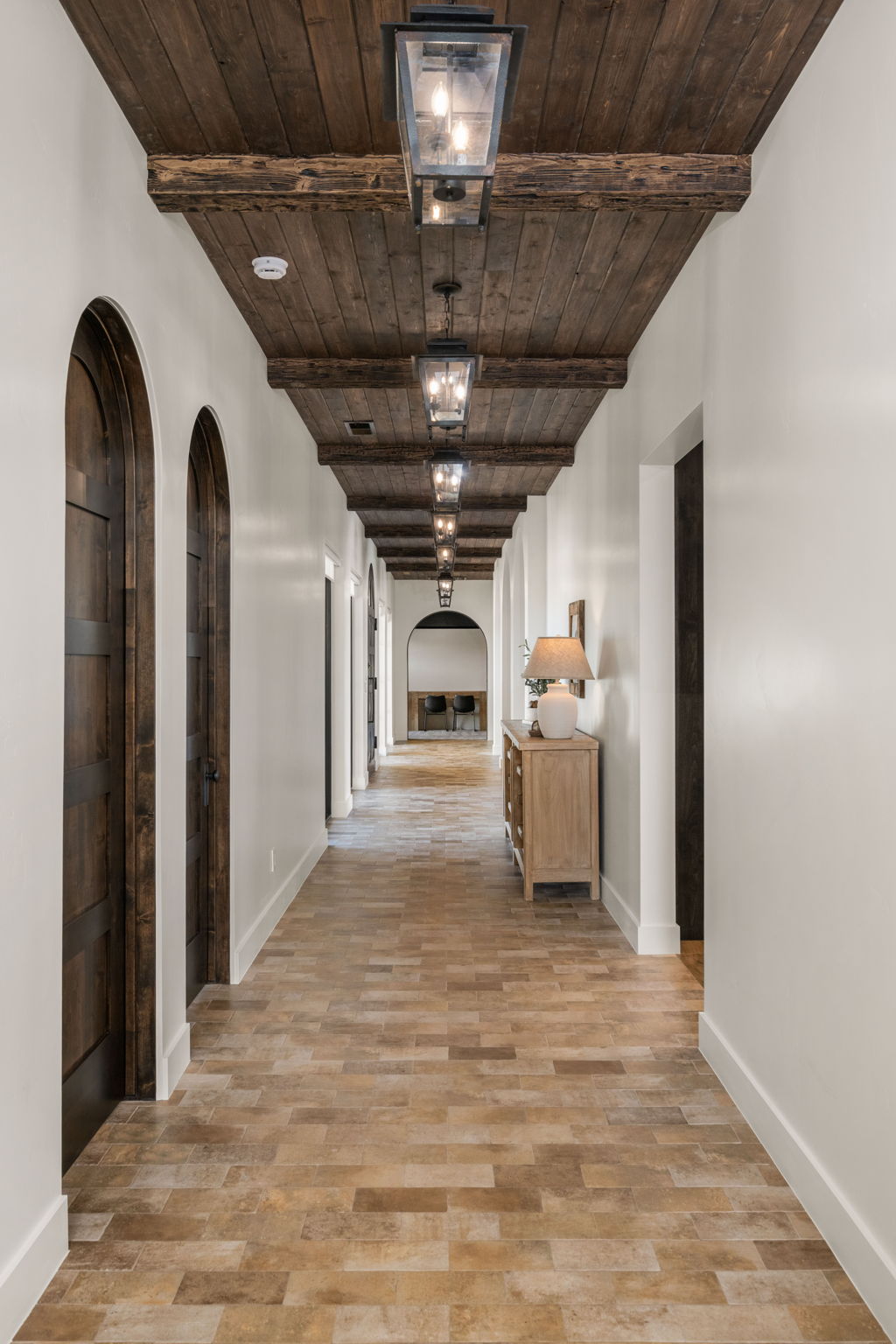 Hall with arched walkways, a wooden ceiling with exposed beams, and light wood-style floors