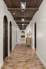 Hall with arched walkways, a wooden ceiling with exposed beams, and light wood-style floors
