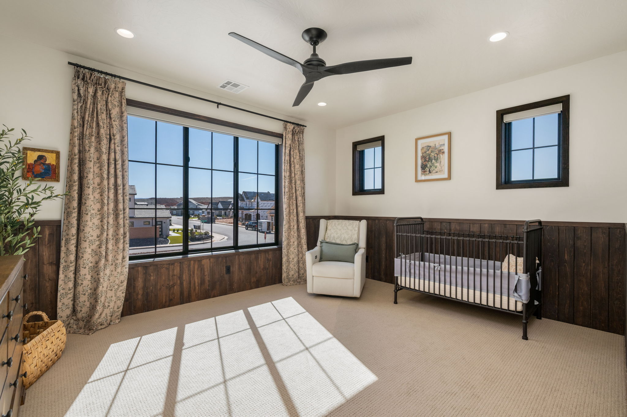 Bedroom featuring a nursery area, light colored carpet, a ceiling fan, a wainscoted wall, and wooden walls