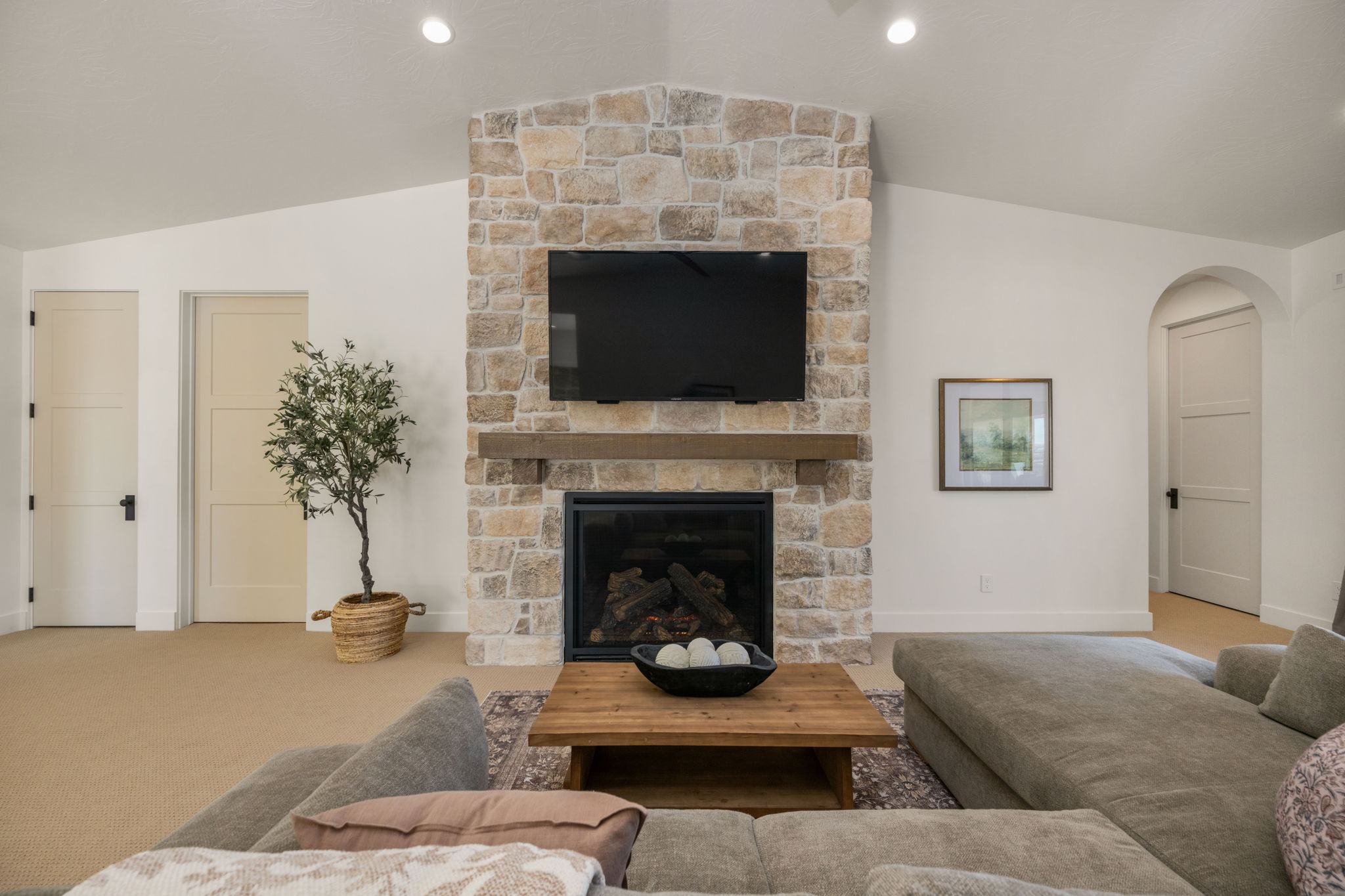 Carpeted living area with arched walkways, vaulted ceiling, and a stone fireplace