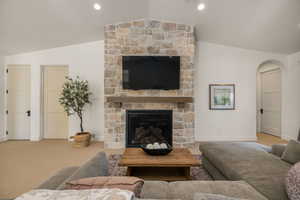 Carpeted living area with arched walkways, vaulted ceiling, and a stone fireplace