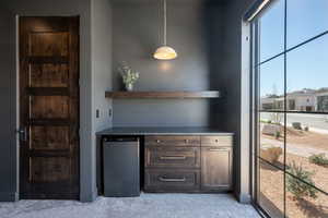 Bar featuring dark wood finish cabinetry, open shelves, stainless steel fridge, and light carpet