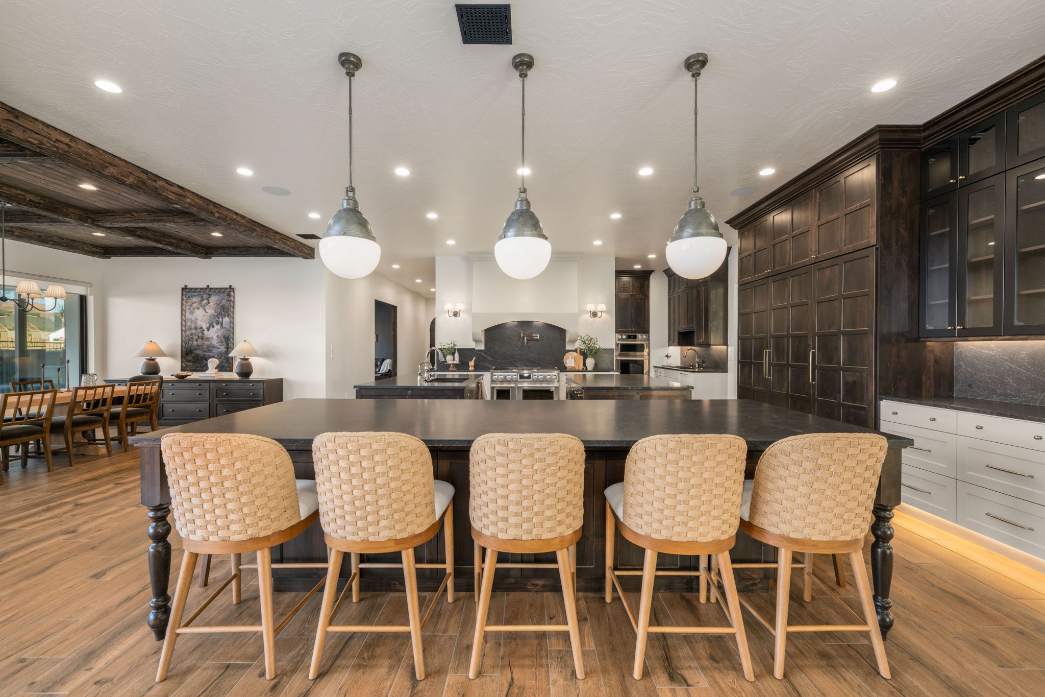 Kitchen with hanging light fixtures, a breakfast bar area, glass fronted cabinets, beam ceiling, and dark stone countertops