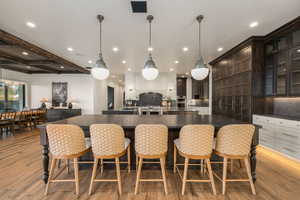 Kitchen with hanging light fixtures, a breakfast bar area, glass fronted cabinets, beam ceiling, and dark stone countertops
