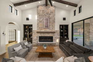 Living area with arched walkways, wood-type flooring, a stone fireplace, and vaulted ceiling
