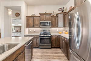 Kitchen with stainless steel appliances, backsplash, dark wood finish cabinets, light wood-style floors, and light stone countertops