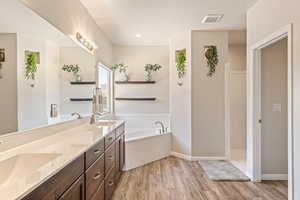 Full bath with a garden tub, a textured ceiling, light wood-style flooring, and double vanity