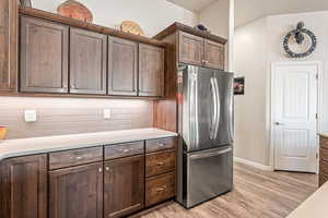 Kitchen featuring freestanding refrigerator, dark wood finish cabinets, light countertops, tasteful backsplash, and light wood-type flooring