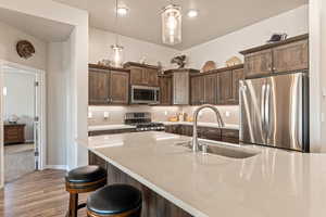 Kitchen with dark wood finish cabinetry, stainless steel appliances, light stone counters, and a kitchen breakfast bar