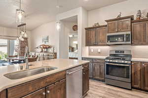 Kitchen featuring stainless steel appliances, dark wood finish cabinets, light wood finished floors, tasteful backsplash, and hanging light fixtures