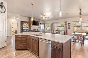 Kitchen with dishwasher, dark wood finish cabinetry, open floor plan, hanging light fixtures, and a fireplace