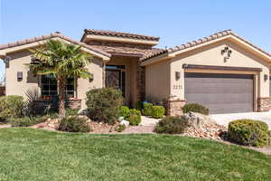 Mediterranean / spanish-style house with stucco siding, stone siding, an attached garage, and a front yard