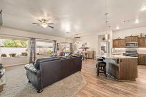 Living room featuring hanging lights, a ceiling fan, a textured ceiling, and light wood-style flooring