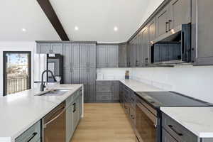 Kitchen with stainless steel appliances, light stone counters, beam ceiling, gray cabinetry, and recessed lighting