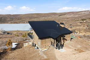 View of home's  lakeview location and exterior featuring a standing seam roof, stone siding, a mountain view, a chimney, and a patio area