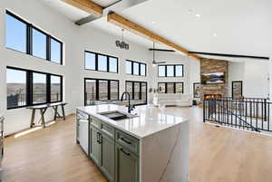 Kitchen featuring a stone fireplace, an island with sink, light wood finished floors, and green cabinetry