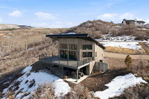 Snow covered back of property featuring a deck with mountain view and a patio area