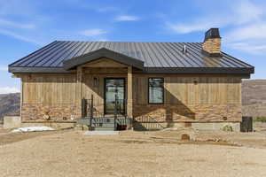View of front facade featuring stone siding, a metal roof, and a chimney