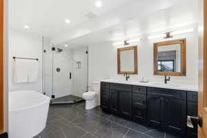 Bathroom with double vanity, a marble finish shower, a freestanding tub, recessed lighting, and dark marble finish flooring