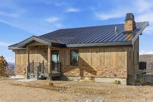 View of front of house featuring stone siding, covered porch, and a metal roof