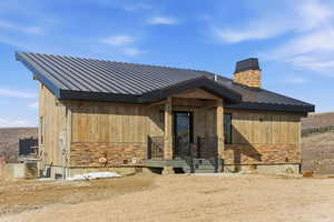 View of front of property featuring stone siding, a metal roof, and a chimney