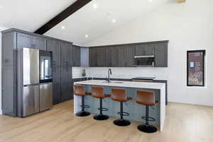 Kitchen featuring stainless steel appliances, light wood-type flooring, a breakfast bar area, a center island with sink, and lofted ceiling