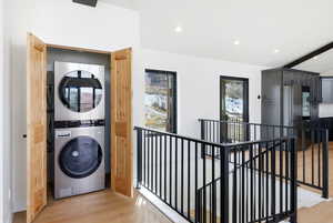 Laundry area with beam ceiling, stacked washer / drying machine, recessed lighting, and light wood-style flooring