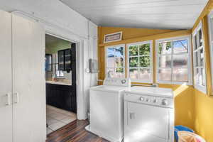 Laundry room with vaulted ceiling, independent washer and dryer, light wood-type flooring, plenty of natural light, and wooden walls