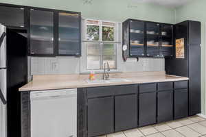 Kitchen featuring freestanding refrigerator, dishwasher, glass fronted cabinets, and light countertops