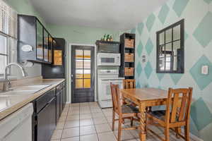Kitchen featuring white appliances, light countertops, light tile patterned flooring, and dark cabinetry
