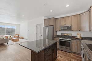 Kitchen featuring stainless steel appliances, dark stone countertops, dark wood finished floors, open floor plan, and a kitchen island