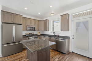 Kitchen featuring stainless steel appliances, dark stone counters, dark wood-type flooring, a center island, and recessed lighting