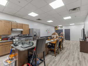 Kitchen with a kitchen island with sink, light stone counters, stainless steel appliances, a paneled ceiling, and a breakfast bar area