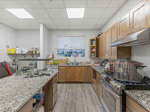 Kitchen with open shelves, stainless steel appliances, light wood-style flooring, light stone countertops, and a paneled ceiling